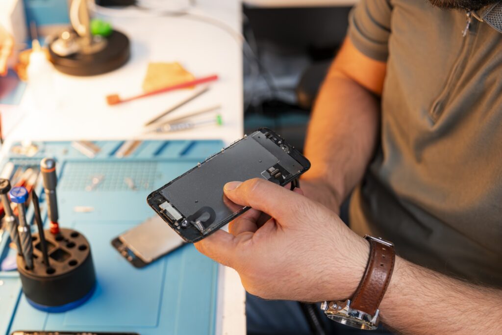 Ali fra MyRepair Aarhus sidder i værkstedet og reparerer en mobil. Close up af Alis hænder der holder en mobil som er skilt ad i forbindelse med reparation.