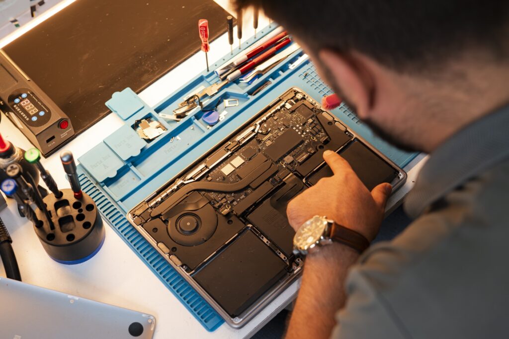 Ali fra MyRepair Aarhus sidder i værkstedet og reparerer en bærbar computer. Close up af Alis hænder der arbejder med en børste for at rengøre indmaden på en laptop.